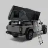 Rear three-quarter view of a Jeep with a black rooftop tent pitched on the bed, extended ladder ready for camping